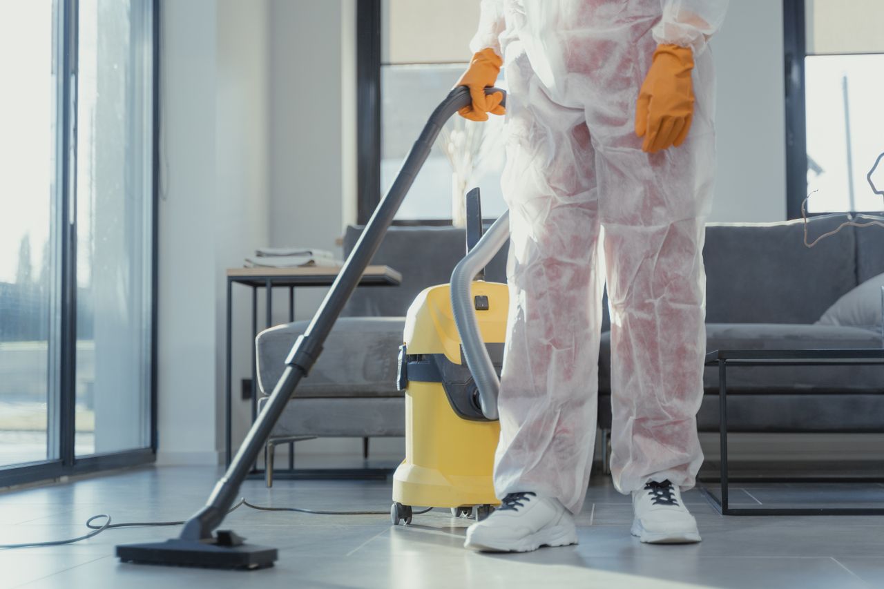 our-story A cleaner in protective coveralls and gloves vacuuming a modern living room.